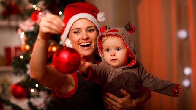 Happy mother showing Christmas ball  to baby near Christmas tree